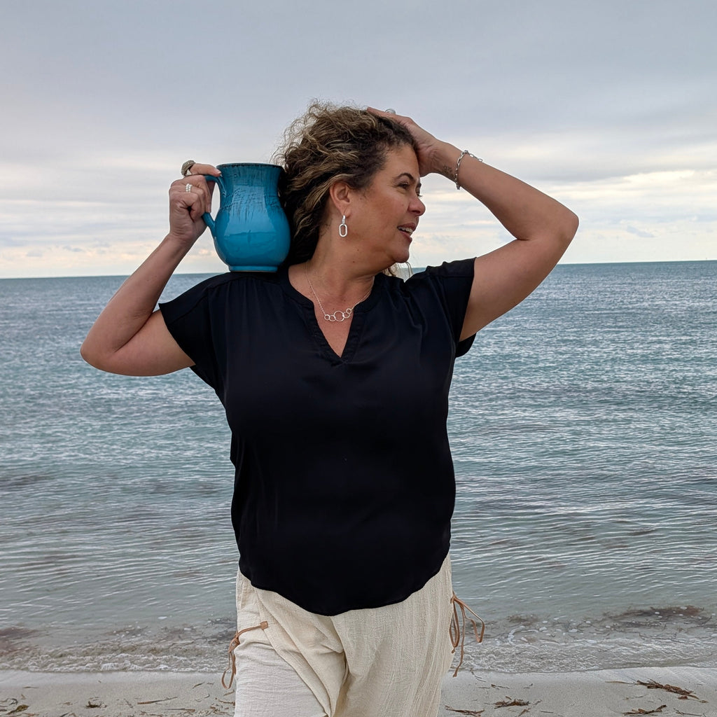 Person standing on a beach holding a blue mug above their head