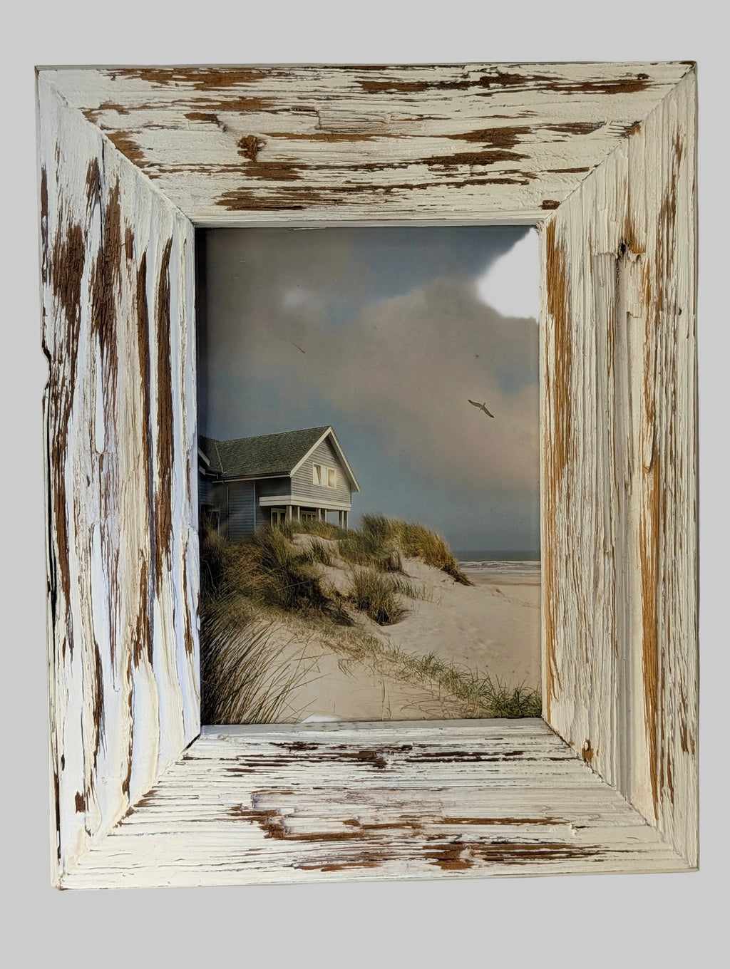 Framed beach scene with a house on a hill, inside a distressed white frame.