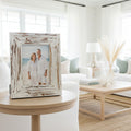 Framed beach scene with a house on a hill, inside a distressed white frame.
